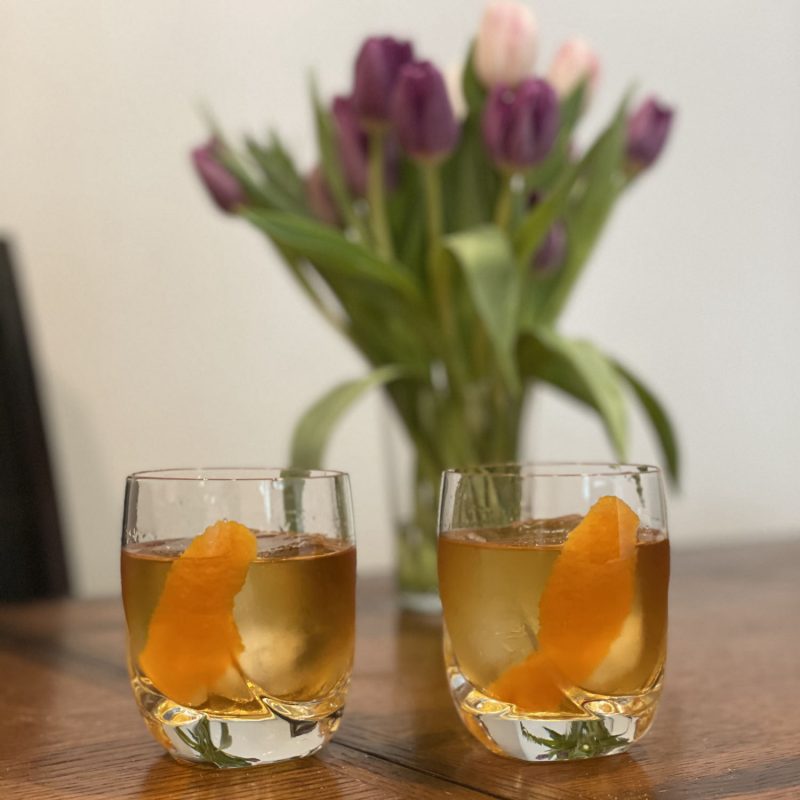 Black tea old fashioned recipe with blurred pink and purple tulips in the background