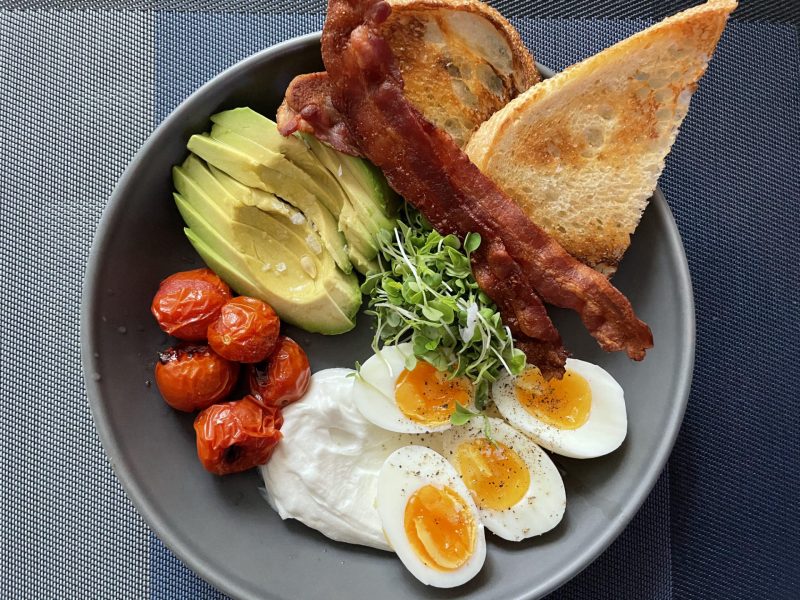 Brunch bowl with grilled tomatoes, microgreens, eggs, avocado and bacon